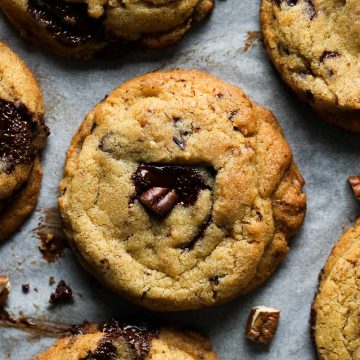 Close up of pecan and chocolate chip cookies with pecan nuts scattered around.