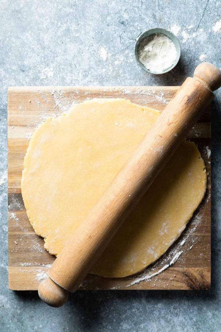 Rolled out shortcrust pastry on a wooden board with a wooden rolling pin.