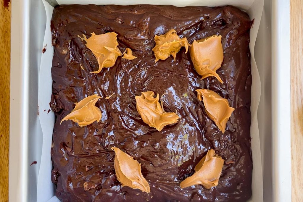 Spoonfuls of Biscoff cookie butter added on top of the brownie batter in the tin.