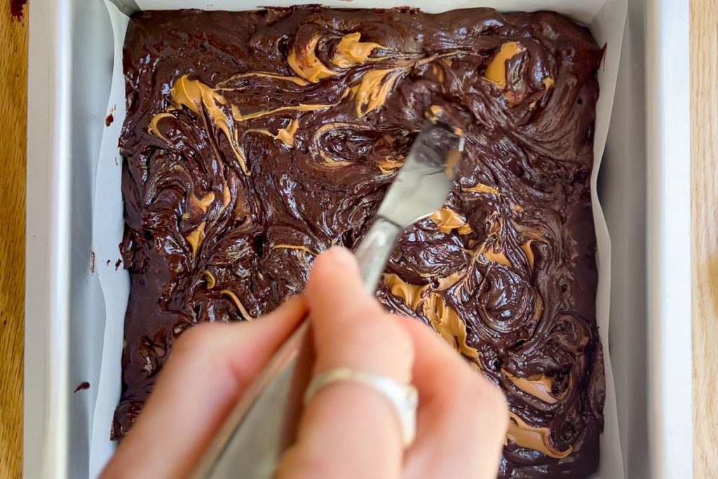 Using a butter knife to swirl the cookie butter on top of the brownies.