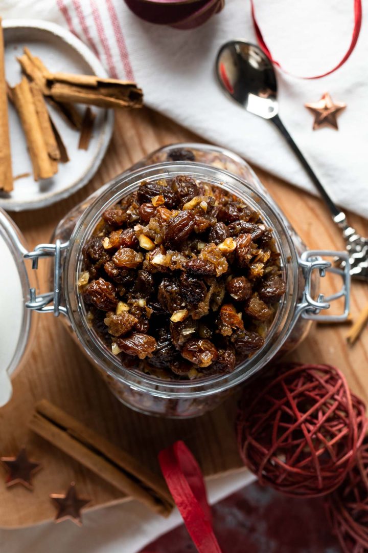 Jar of mincemeat (fruit mince) surrounded by spices and Christmas decorations.