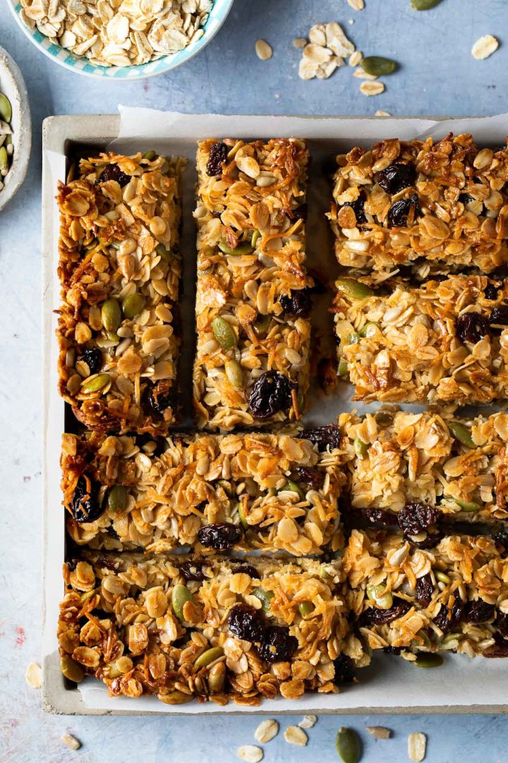 overhead photo of muesli bars in a square dish, with oats and seeds scattered around the sides.
