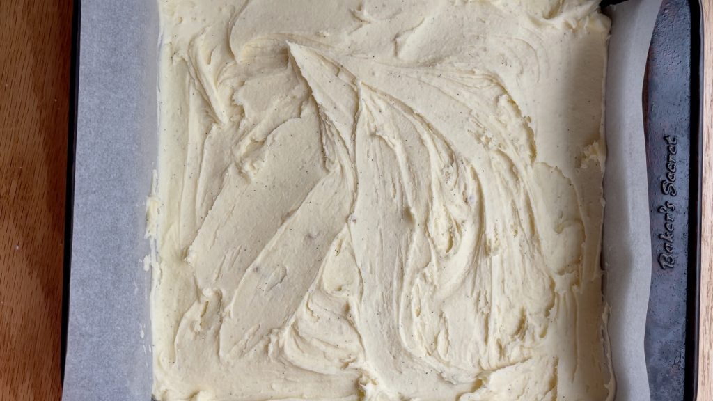 The buttercream layer spread over the Nanaimo base in the tin.