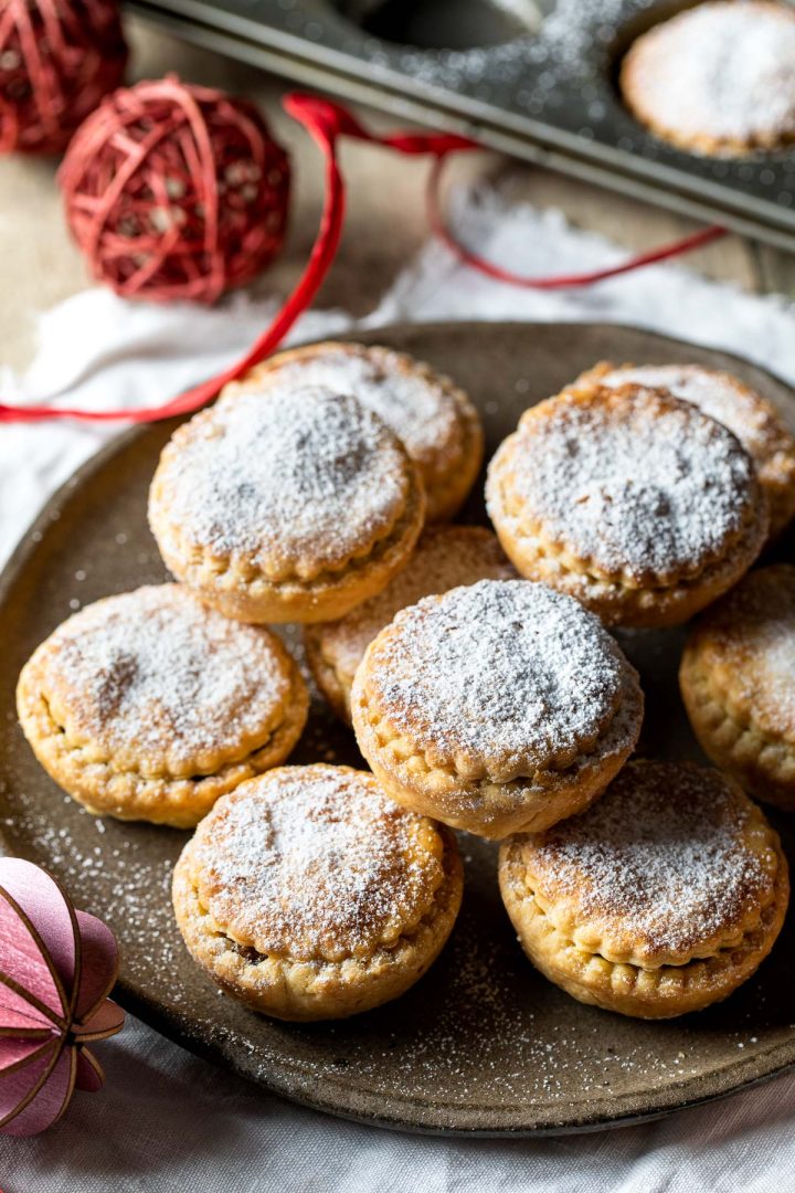 Side view of a plate piled high with mince pies and dusted with icing sugar.