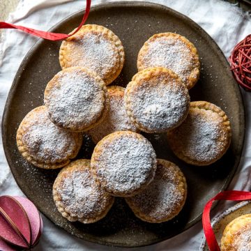 Shortcrust mince pies on a plate dusted with icing sugar.