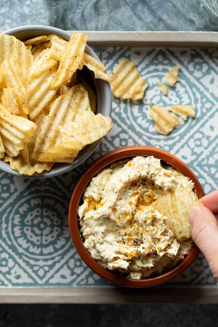 A hand dipping a potato chip into the dip.