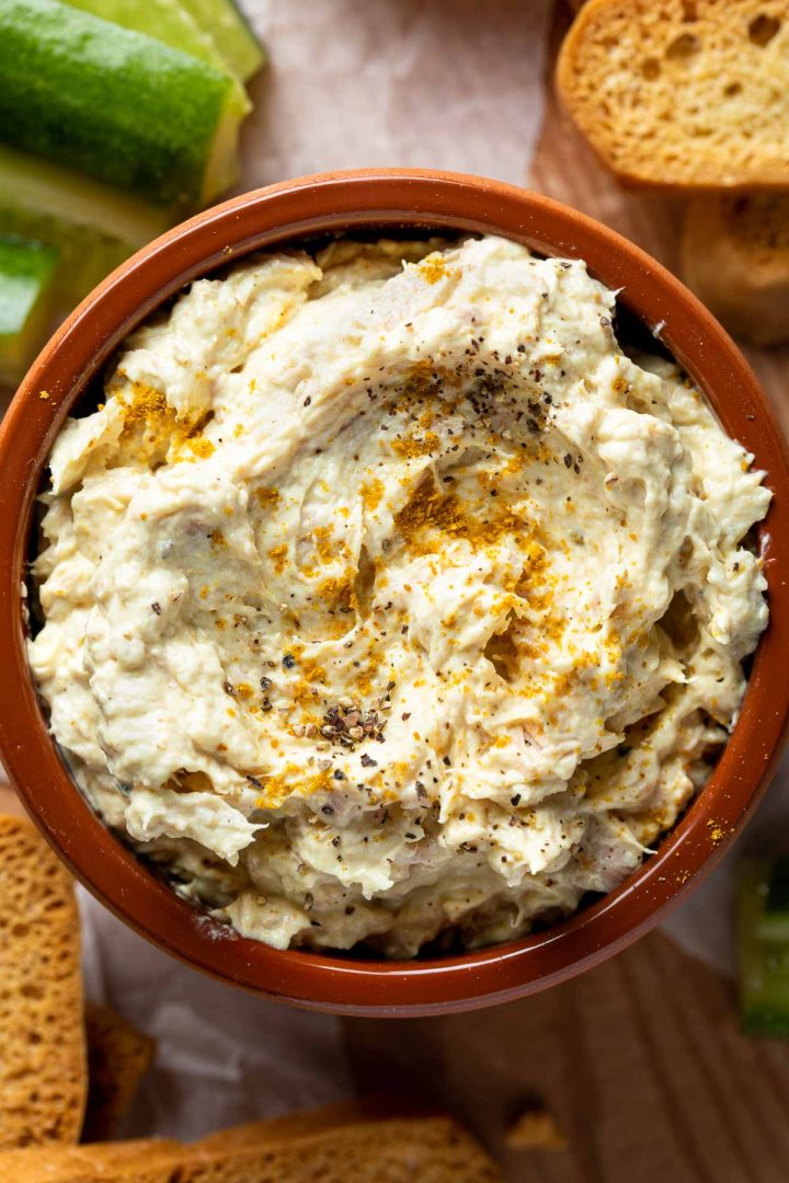 Close up of tuna dip served in a dish surrounded with cucumbers and bread.