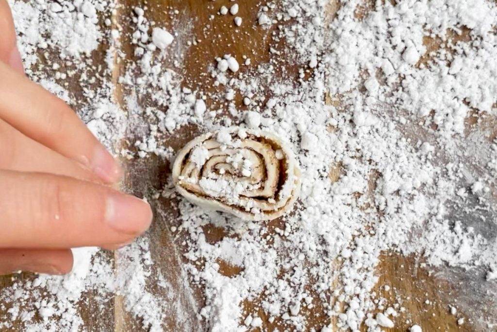 A slice of cinnamon puff pastry on a wooden board dusted with icing sugar.