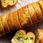 Baguette garlic bread on a wooden board with some slices on their side to show the buttery filling.