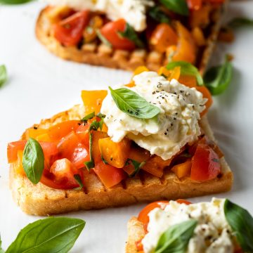 Close up of a bruschetta topped with burrata cheese and tomatoes.