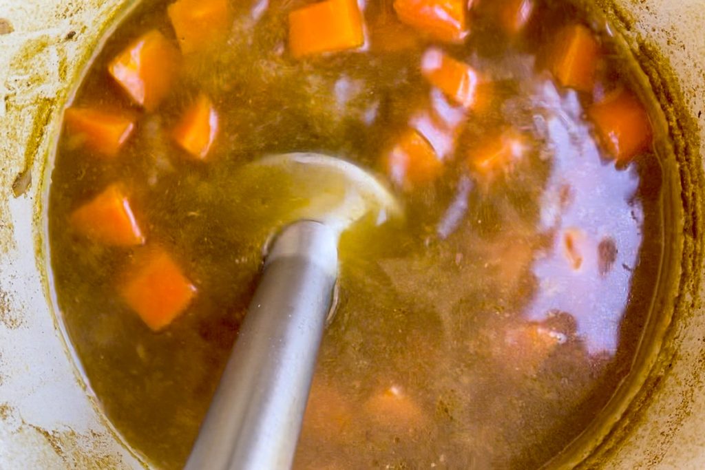 A stick blender blending the cooked soup.