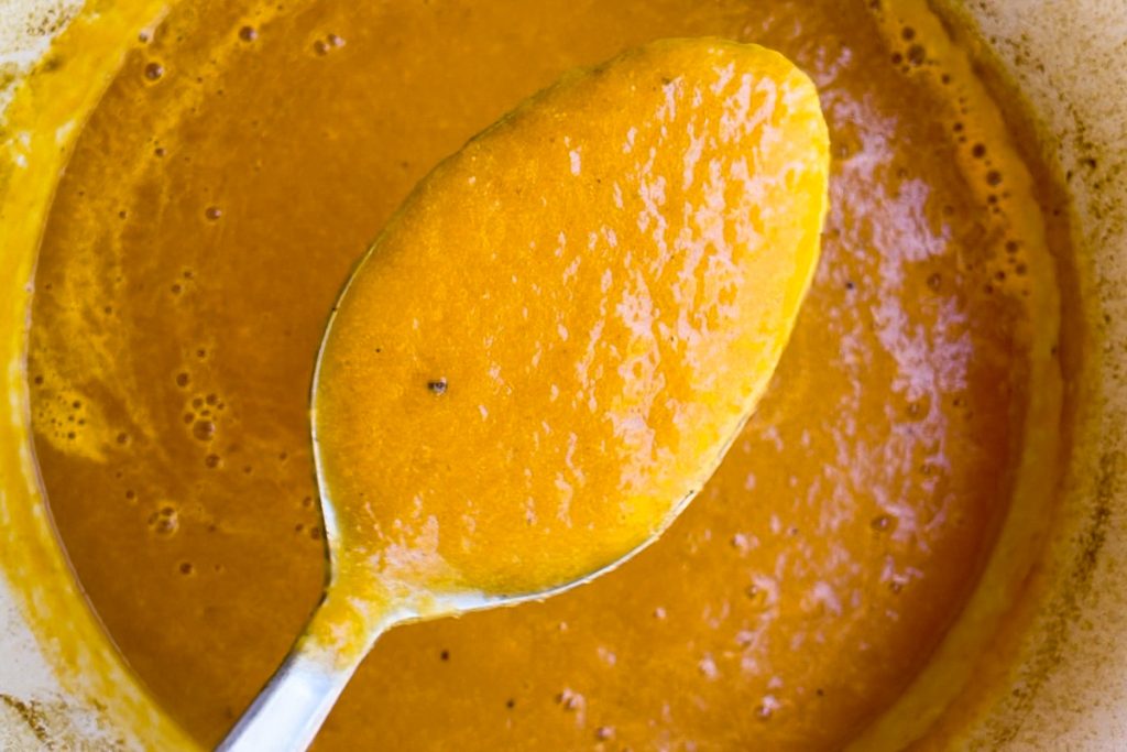 A spoon holding up a spoonful of the soup to show the smooth texture.