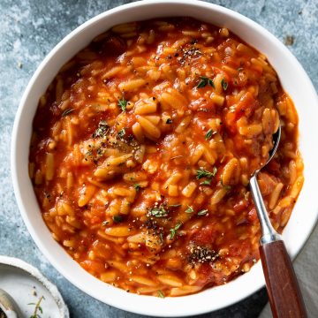 A bowl of Greek orzo in tomato sauce with a spoon in the bowl ready to eat.