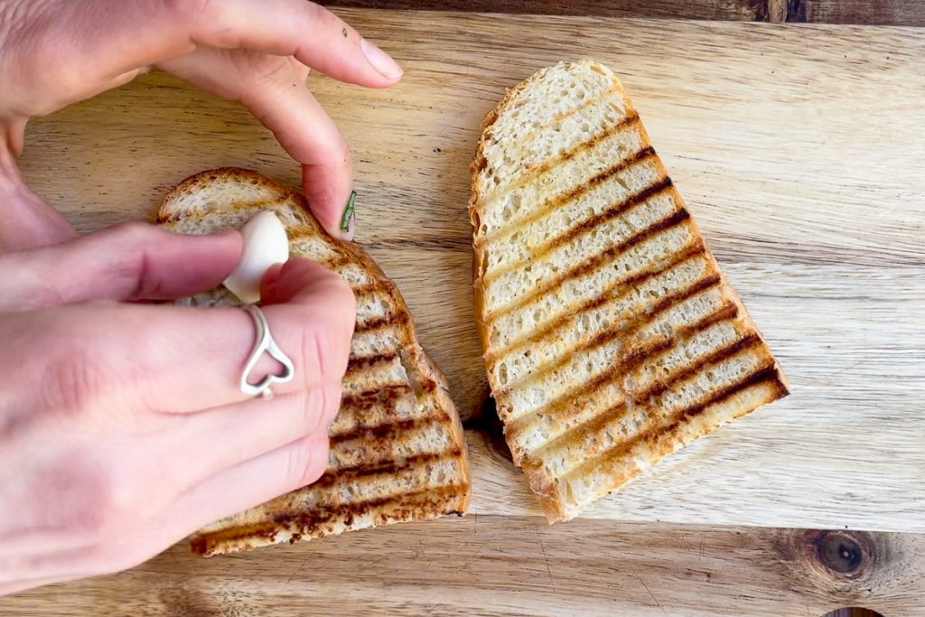 The grilled bruschetta toasts being rubbed with fresh garlic.