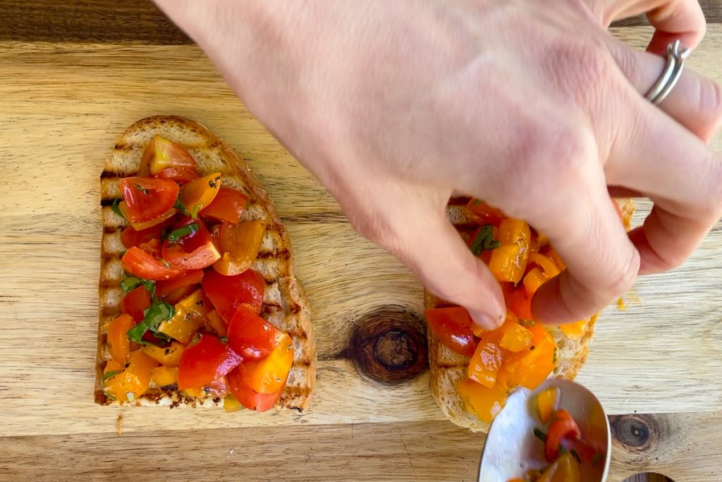 The bruschetta being topped with chopped tomatoes.