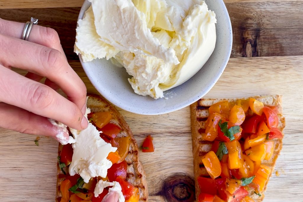 The tomato bruschetta being topped with torn burrata.