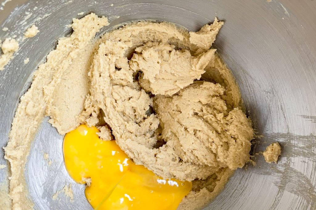 The creamed butter and sugars in a stand mixer bowl with beaten egg added.