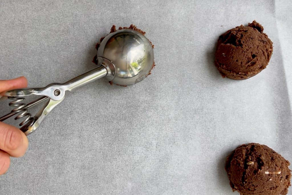An ice cream scoop used to place balls of the chocolate cookie dough on a lined baking sheet.