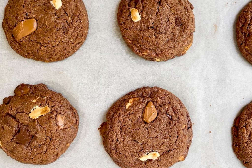 Freshly baked triple chocolate chunk cookies on lined baking sheet.