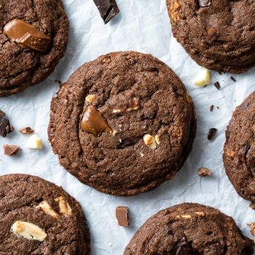 Triple chocolate cookies on a white background sprinkled with milk, dark and white chocolate.
