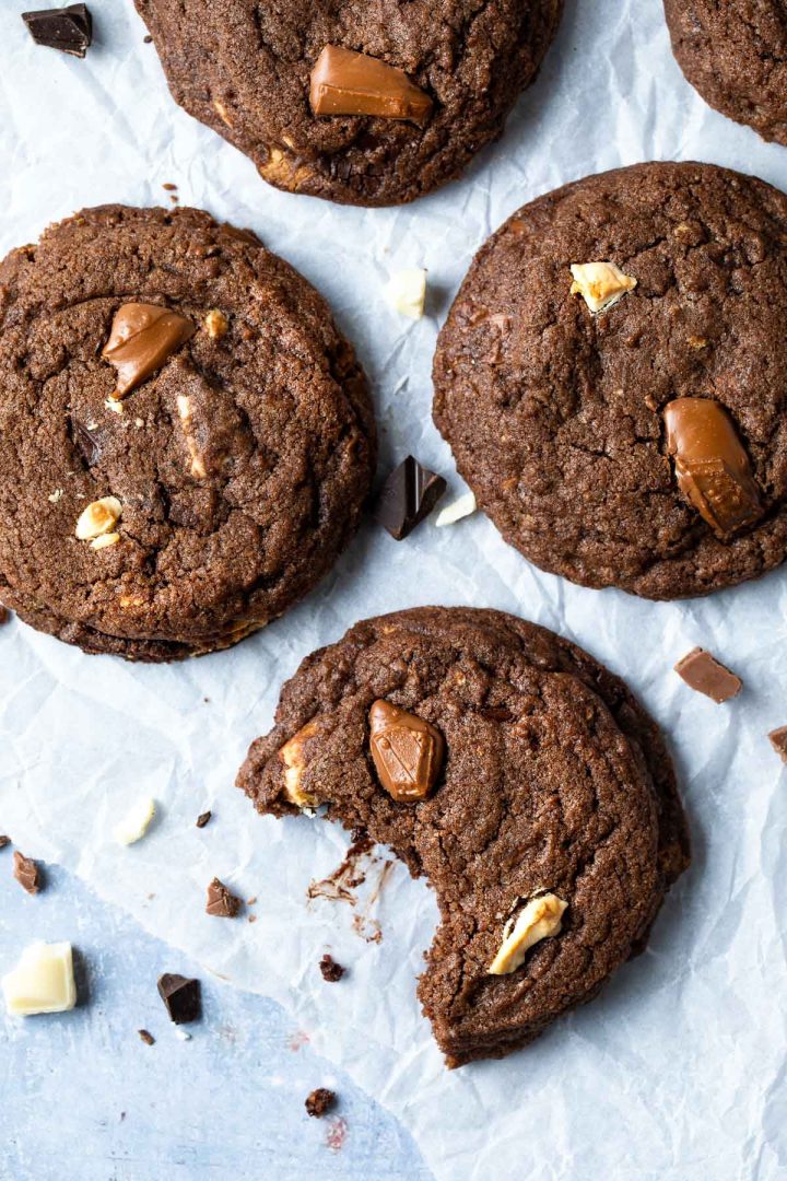 A triple chocolate chip cookie with a bite taken out to show the melted chocolate chunks.