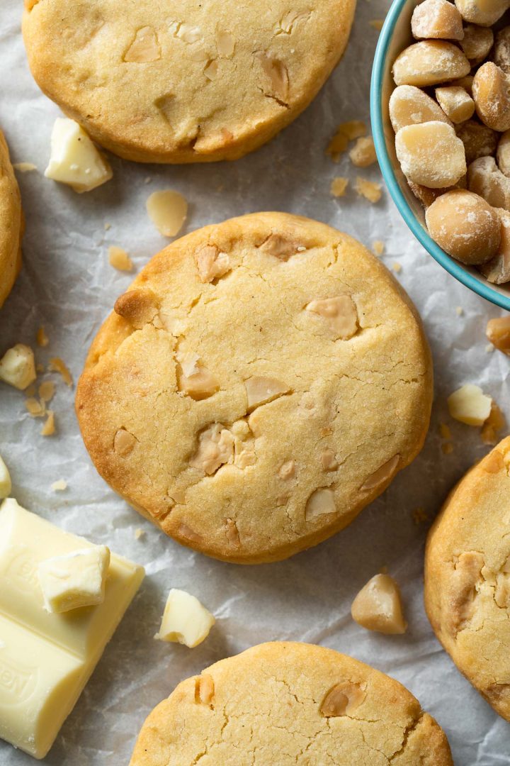 Close up of a white chocolate and macadamia nut cookie, with chunks of white chocolate and macadamia nuts just visible around the sides.