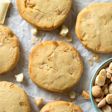 White chocolate macadamia cookies on a white background with white chocolate chunks and macadamia nuts scattered around.