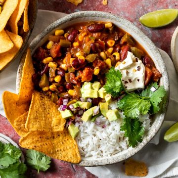 A bowl of Mexican chilli sin carne served with corn chips, rice, avocado and sour cream