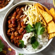 slow cooker chilli con carne in a bowl with rice and corn chips, topped with grated cheese, sour cream fresh corainder.