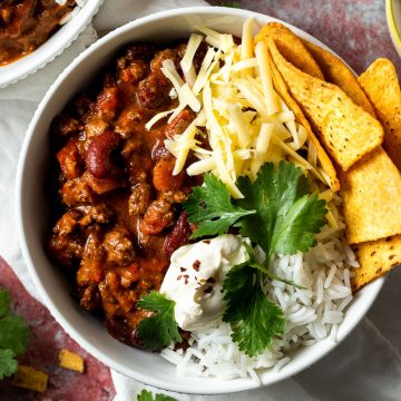 slow cooker chilli con carne in a bowl with rice and corn chips, topped with grated cheese, sour cream fresh corainder.