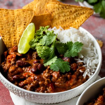 A bowl of slow cooker chilli con carne served with rice and corn chips.