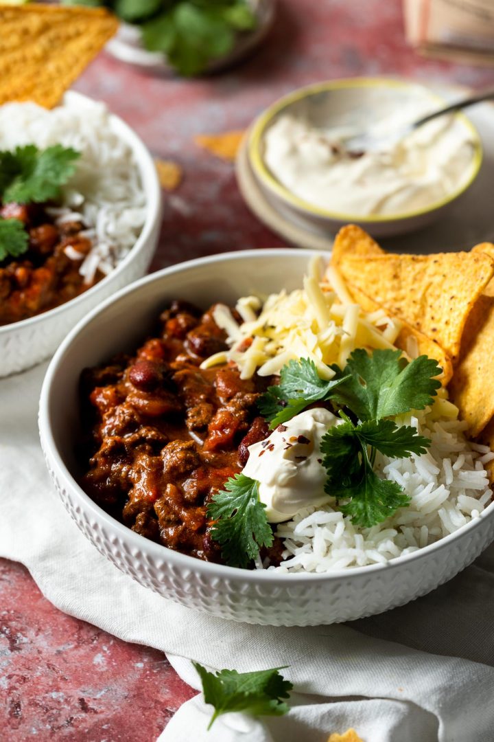 Two bowls of slow cooker chili with rice and corn chips.