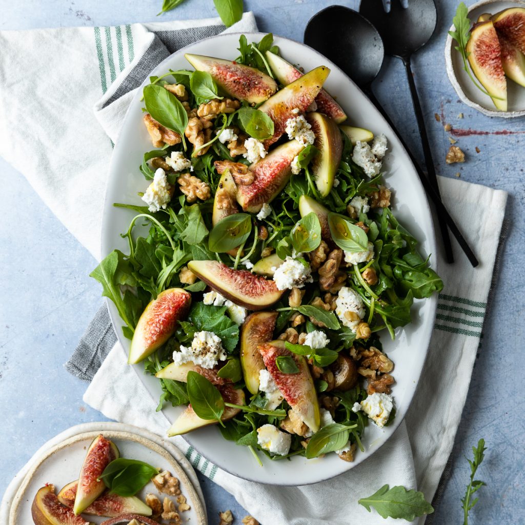 Fig goats cheese salad on white serving plate with extra figs just visible in the top and bottom corners.