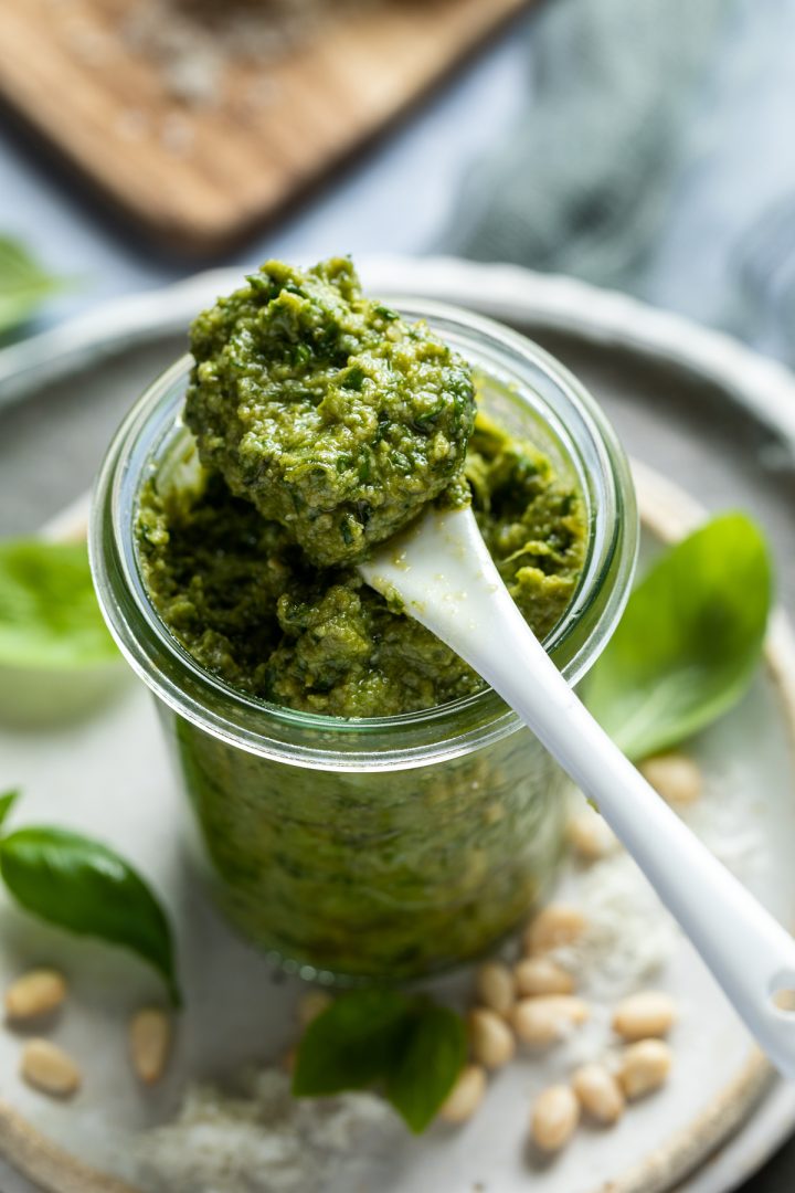 Pesto in a glass jar with a spoon holding a spoonful balanced on top of the jar.