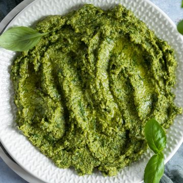 Basil pesto on a white plate topped with fresh basil leaves.