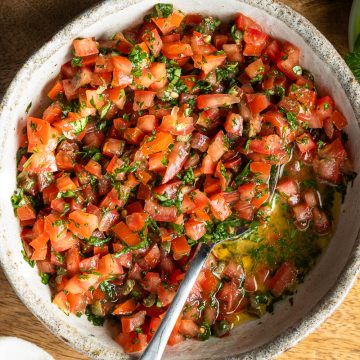 Prepared sauce vierge in a bowl with a spoon, fresh herbs just visible in the top right corner.