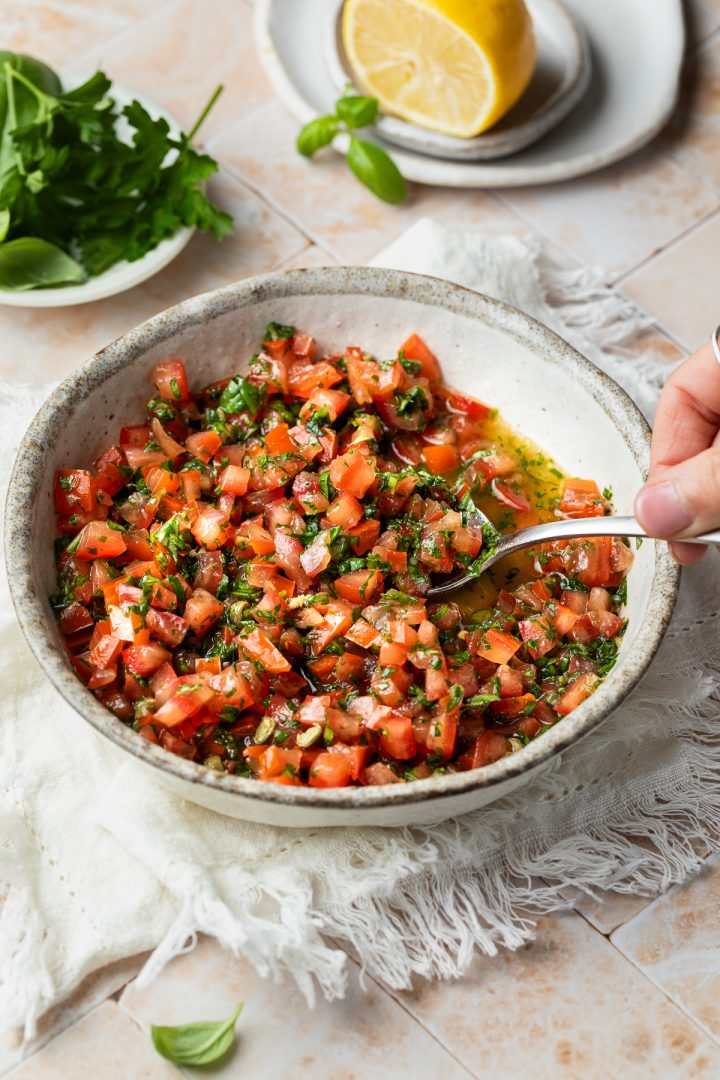A hand holding a spoon ready to serve the tomato vinaigrette.