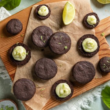 Chocolate lime cookies on a wooden board, with fresh limes and citrus leaves dotted around the edges.