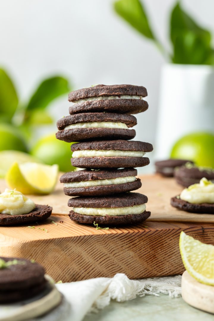 A stack of 5 chocolate cookies filled with lime buttercream, with fresh limes just visible behind.