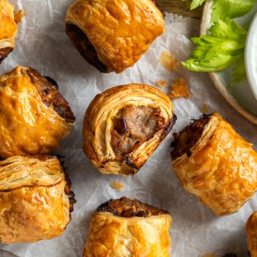 Multiple puff pastry sausage rolls on a board, some on their sides to show the filling.