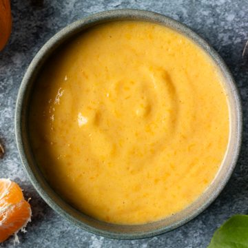 A blue bowl of mandarin curd with fresh mandarin segments dotted around it.