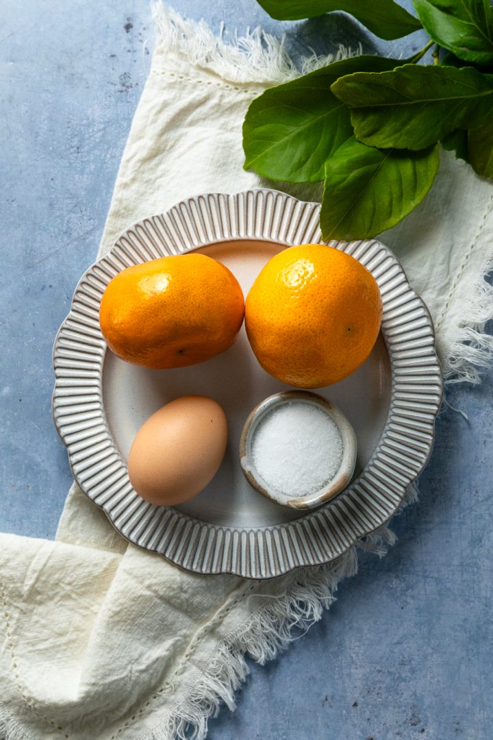 Mandarins, an egg and sugar on a plate.