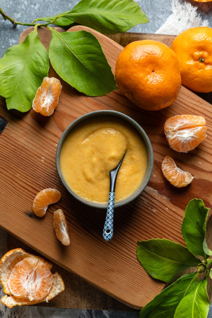 A bowl of mandarin curd with a spoon ready to serve, fresh mandarins arranged around the bowl.
