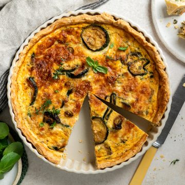Courgette quiche in the pie tin with a portion cut out.