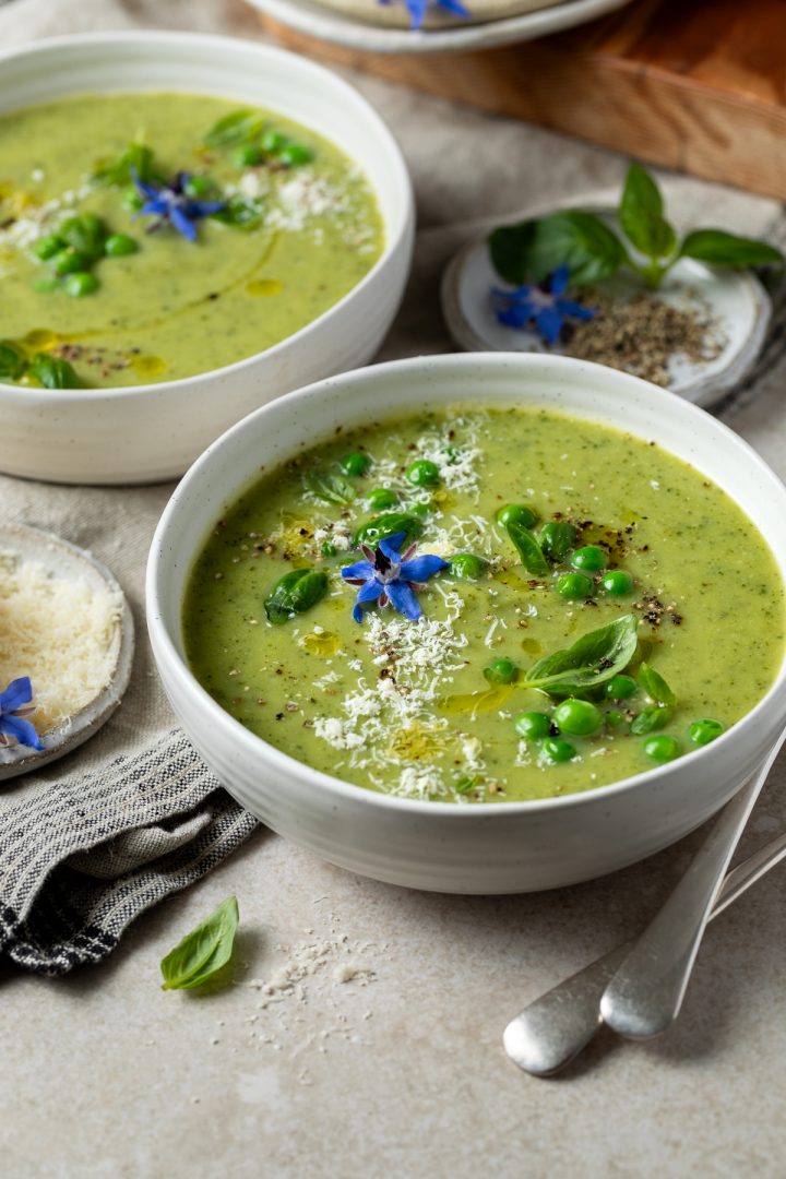 Two bowls of courgette soup with peas, parmesan and basil.