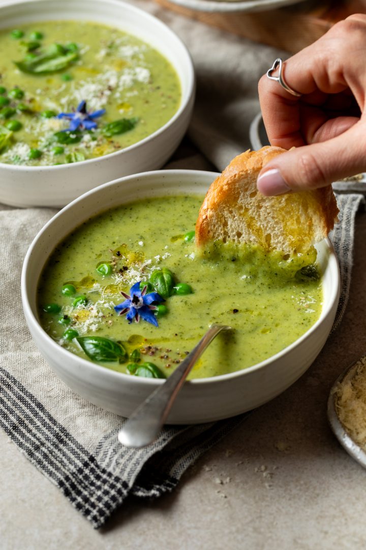 A hand dunking a slice of toast into a bowl of courgette soup.