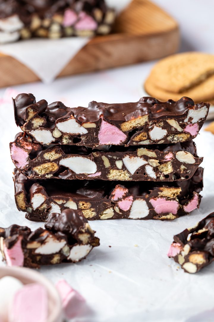 A stack of pieces of chocolate rocky road with marshmallows and biscuit crumbs scattered around.