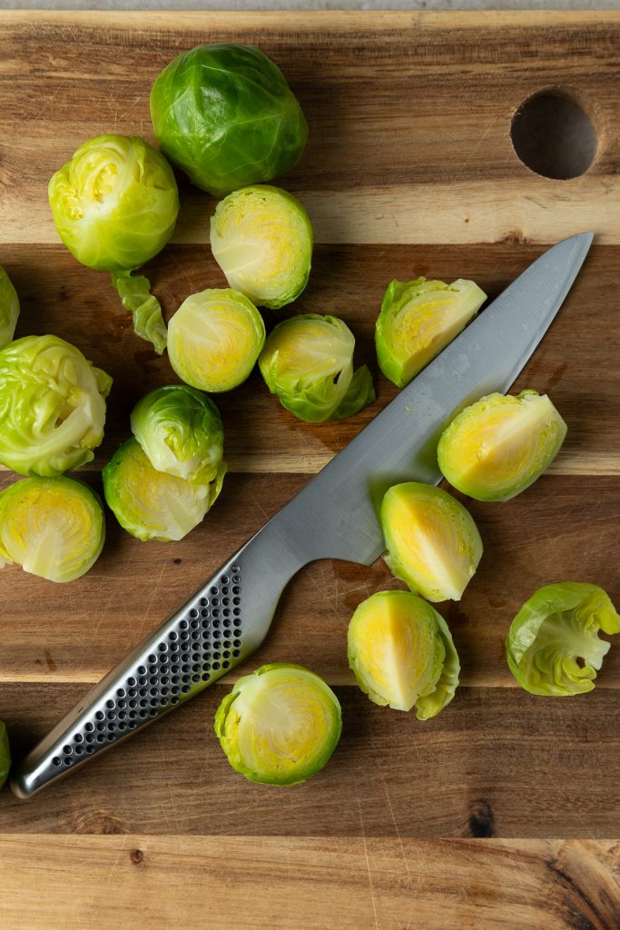 Blanched Brussels sprouts on a board with a knife.