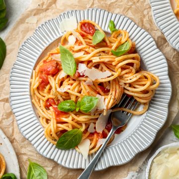 A plate of pasta al pomodoro topped with parmesan shavings and basil leaves.