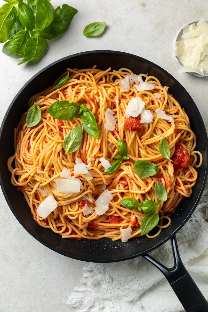 The finished tomato spaghetti in a pan topped with fresh basil and parmesan.